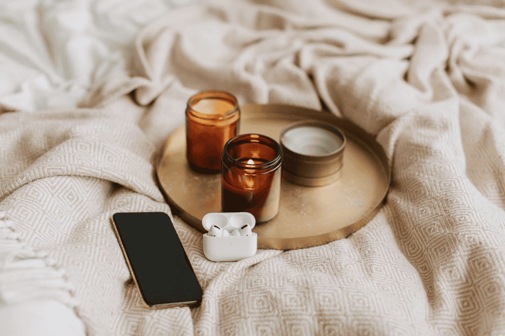 Cozy bed with candles, a phone, and AirPods, symbolizing a peaceful environment for overcoming goal setting anxiety and perfectionism.