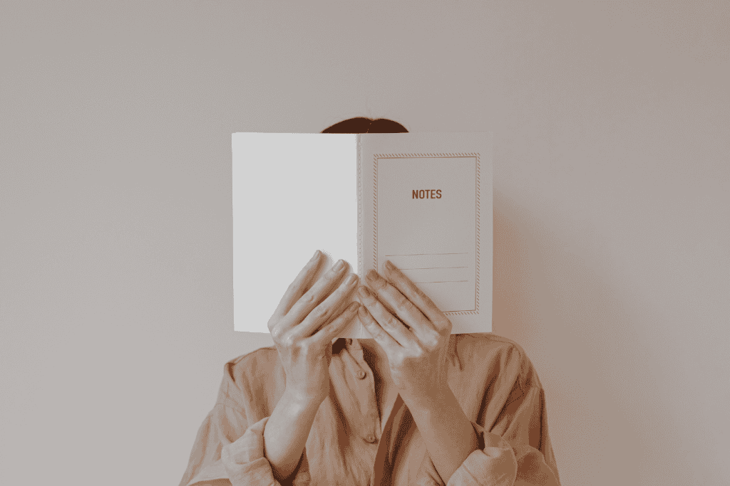 A woman hiding behind a notebook, symbolizing the struggle of setting boundaries and protecting personal space as a recovering people-pleaser.