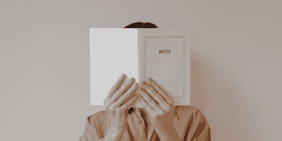 A woman hiding behind a notebook, symbolizing the struggle of setting boundaries and protecting personal space as a recovering people-pleaser.