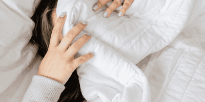 A woman lying in bed, covering her face, struggling with comfort zone anxiety and the overwhelming feeling of staying stuck.