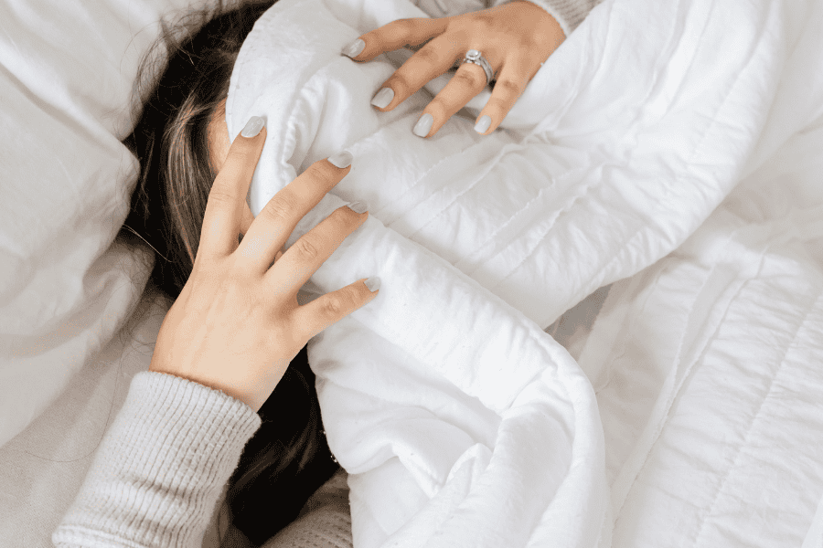 A woman lying in bed, covering her face, struggling with comfort zone anxiety and the overwhelming feeling of staying stuck.
