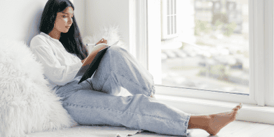 A woman sitting and writing, reflecting on the difference between therapy vs self-help and how each can support personal growth.