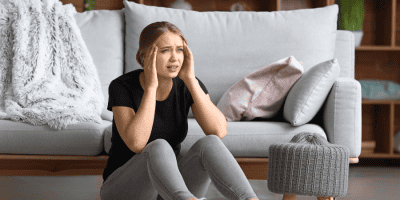 Young woman sitting on floor struggling with anxiety and wondering how to stop a panic attack.