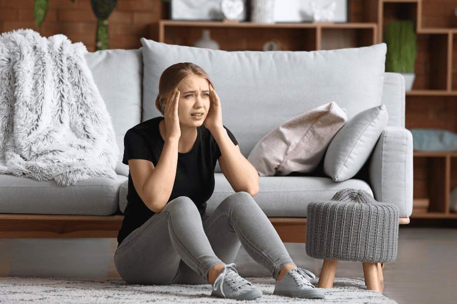 Young woman sitting on floor struggling with anxiety and wondering how to stop a panic attack.
