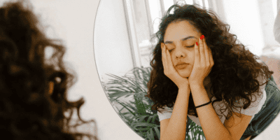 Young woman staring at her reflection with her hands on her face, unsure if she's feeling anxiety or intuition.