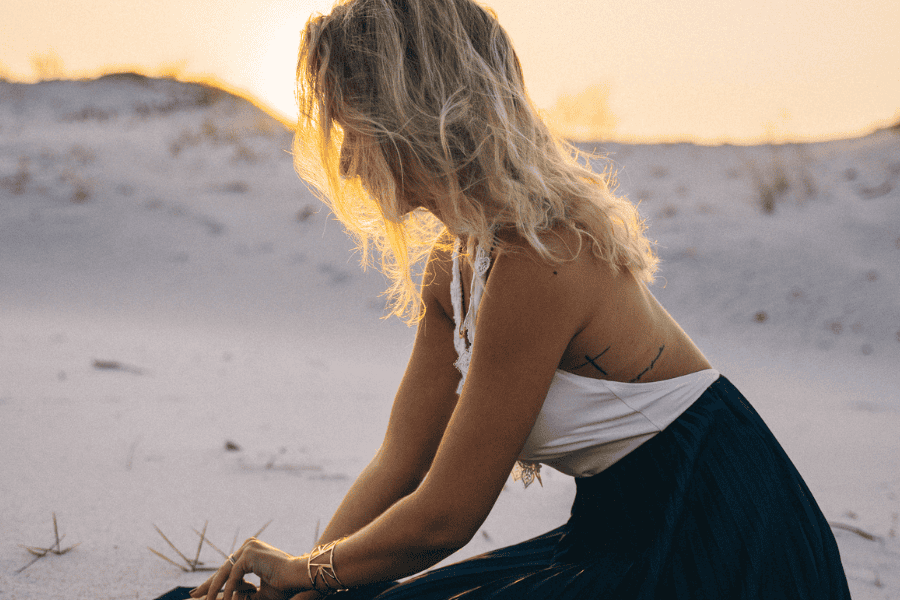 Woman sitting quietly in the sand at sunset, reflecting with a sense of anxiety or intuitive awareness.
