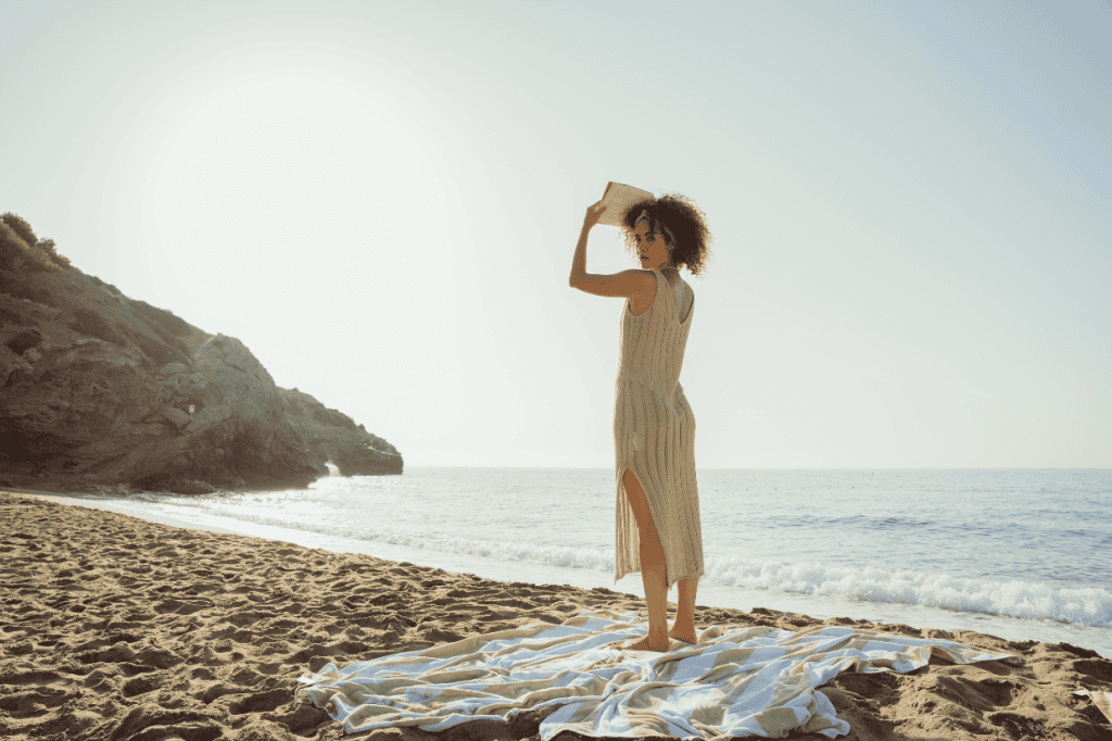 Woman standing with a book on her head, looking back at the ocean, symbolizing self-awareness and exploring why trauma affects confidence.