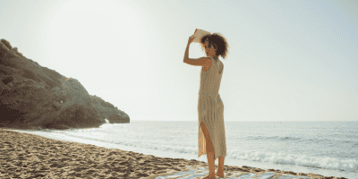 Woman standing with a book on her head, looking back at the ocean, symbolizing self-awareness and exploring why trauma affects confidence.