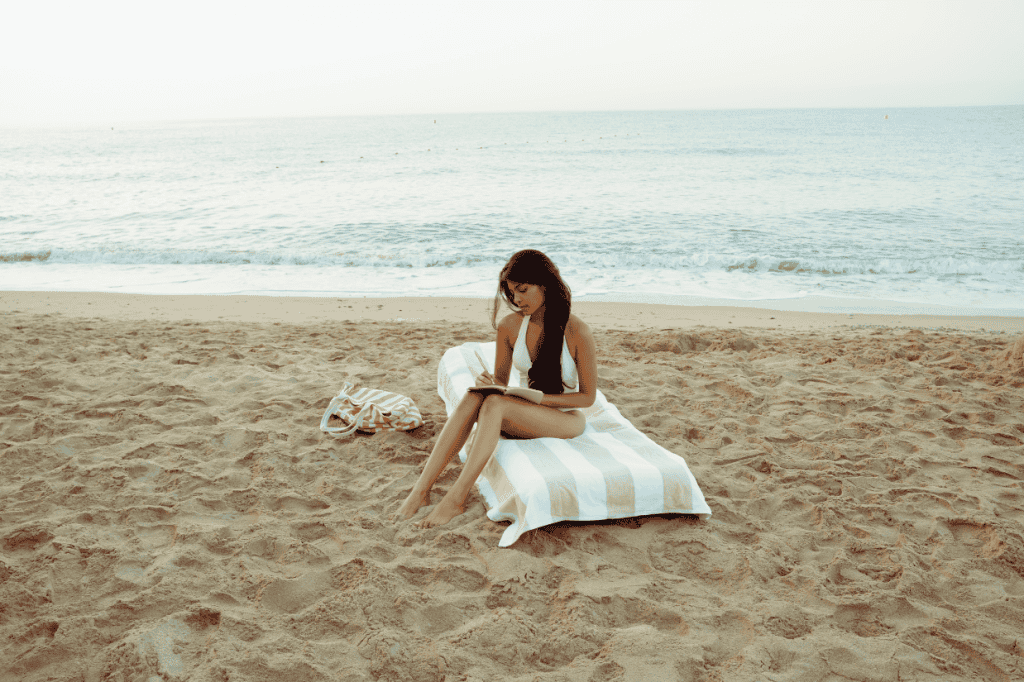 Close-up of a woman sitting on the sand near the water, grounding herself as she works to regain self trust after trauma.