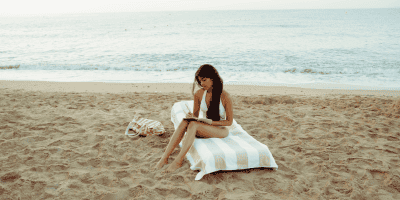 Close-up of a woman sitting on the sand near the water, grounding herself as she works to regain self trust after trauma.