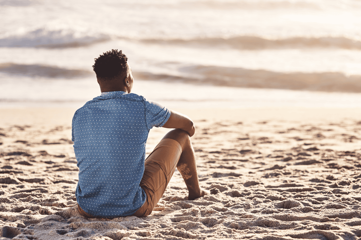 Person sitting alone on the beach at sunset, reflecting quietly and reconnecting with yourself through stillness and mindfulness.