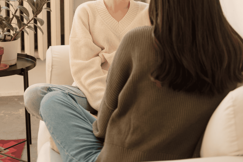 Two friends talking on a couch about personal challenges, reflecting the experience of wondering why you feel responsible for other people’s emotions.